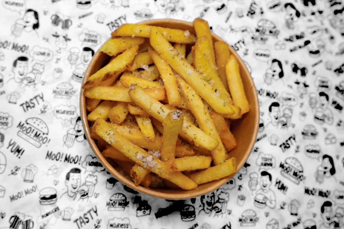 A MooMoo Burger sides bundle featuring golden thick-cut fries, and creamy coleslaw with crispy onions. Presented together on MooMoo Burger’s “Moo! Moo!” illustrated greaseproof paper in Hackney, London. Drinks also includes beers