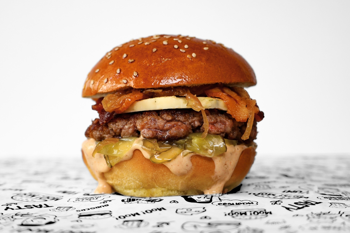 A MooMoo Burger sides bundle featuring golden thick-cut fries, and creamy coleslaw with crispy onions. Presented together on MooMoo Burger’s “Moo! Moo!” illustrated greaseproof paper in Hackney, London. Drinks also includes beers